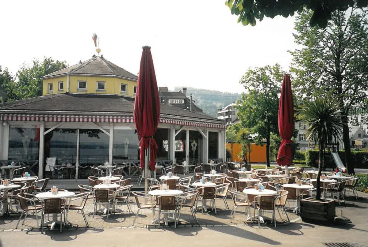 Der Pavillon mit vollem Gastgarten und roten Sonnenschirmen